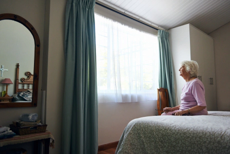 femme âgée assise sur un lit et regarde par la fenêtre