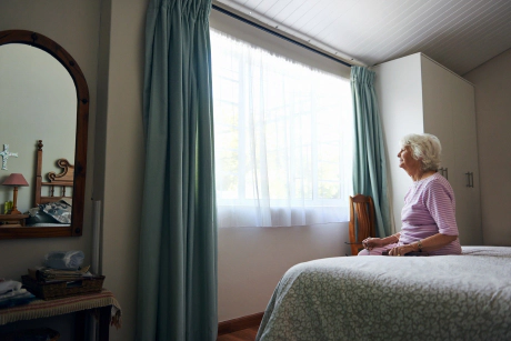 Femme âgée seule femme âgée assise sur un lit et regarde par la fenêtre