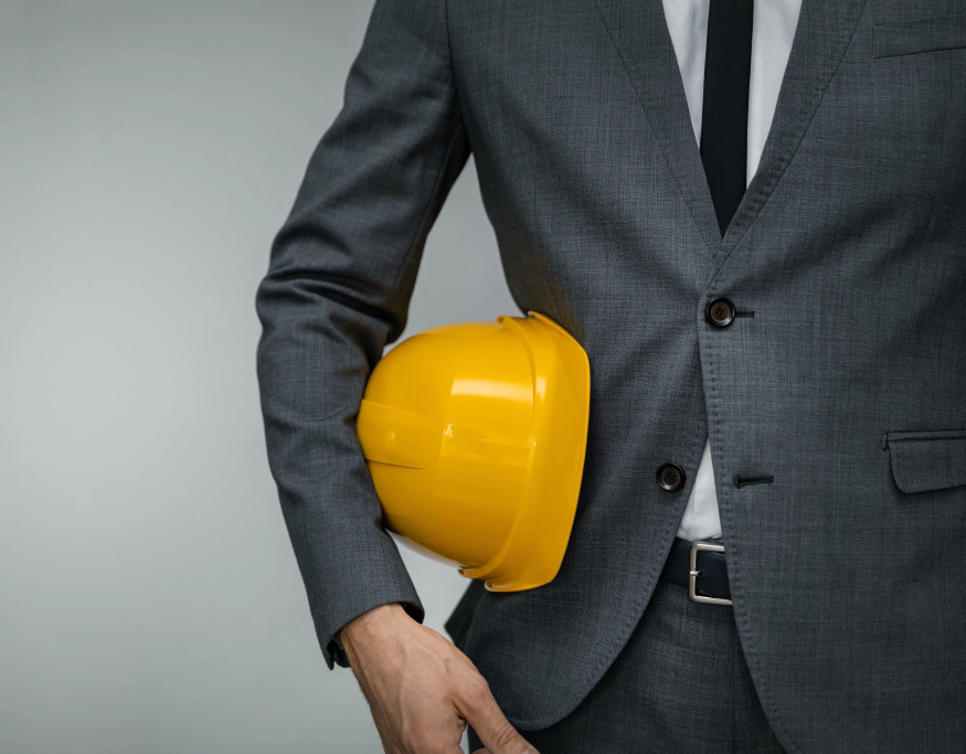 homme en costard gris tient un casque jaune dans les mains